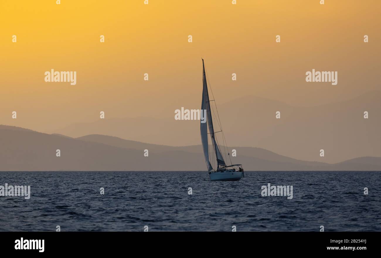 Barca a vela in mare aperto all'ora d'oro di sera. Montagne Silhouette sullo sfondo. Avventura estiva, vacanza attiva nel Mar Mediterraneo Foto Stock