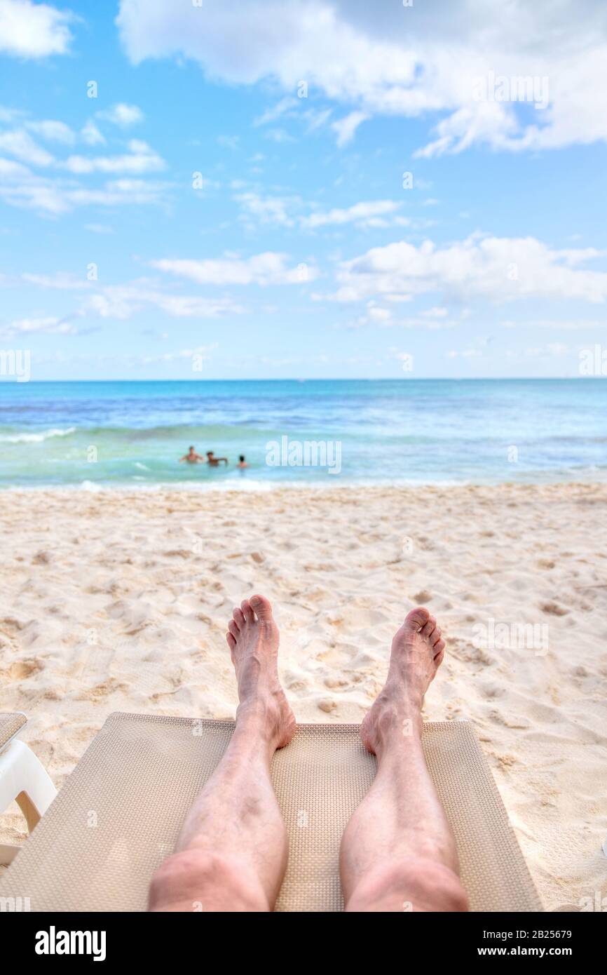 La prospettiva personale dell'uomo che si rilassa su una poltrona sulla spiaggia di sabbia con vista dei piedi verso la vista del mare e dello spazio delle copie. Scatto preso nei coa caraibici Foto Stock