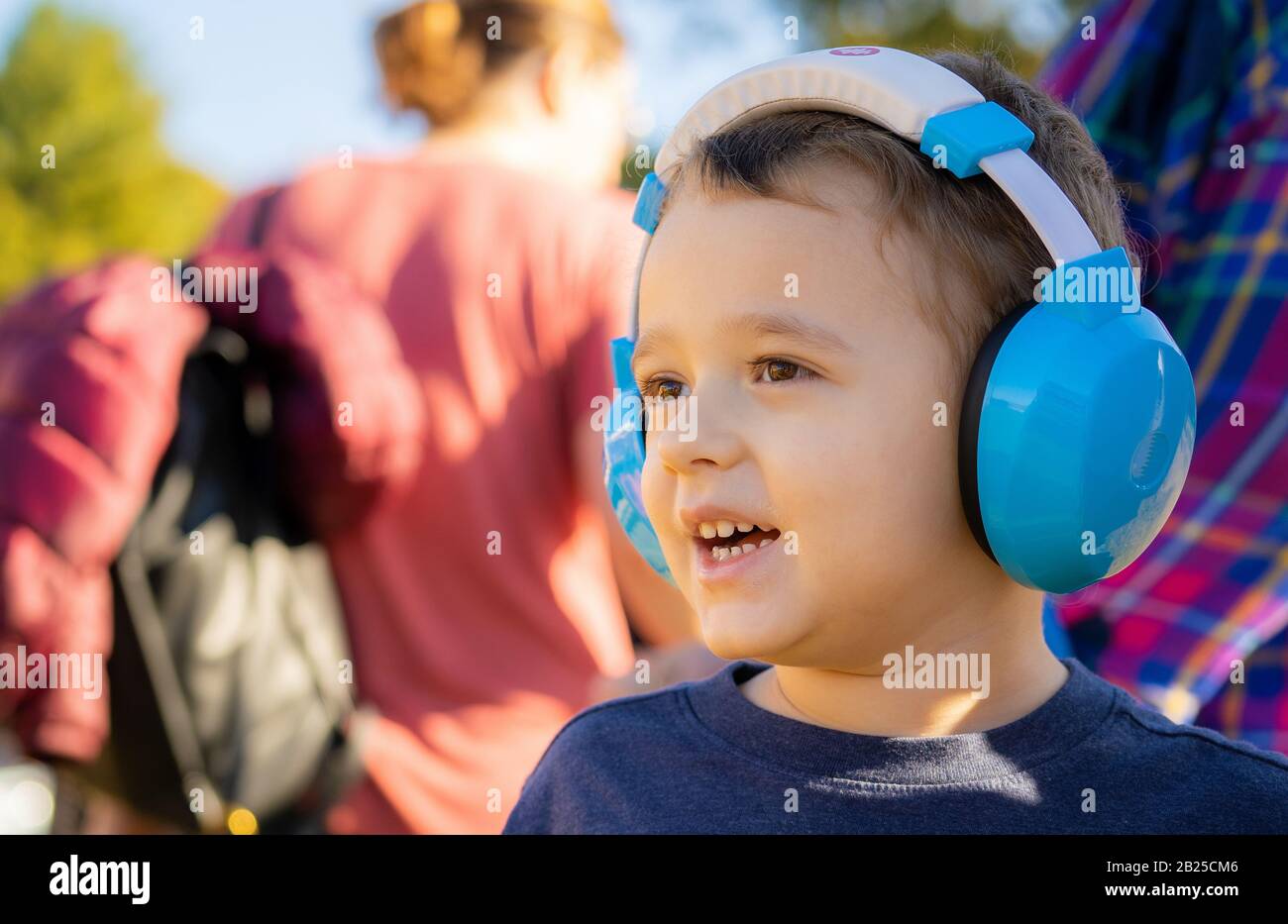 Ragazzo autistico con le cuffie all'esterno, guardando avanti, sorridente. Cielo blu, autunno, ritratto. Foto Stock