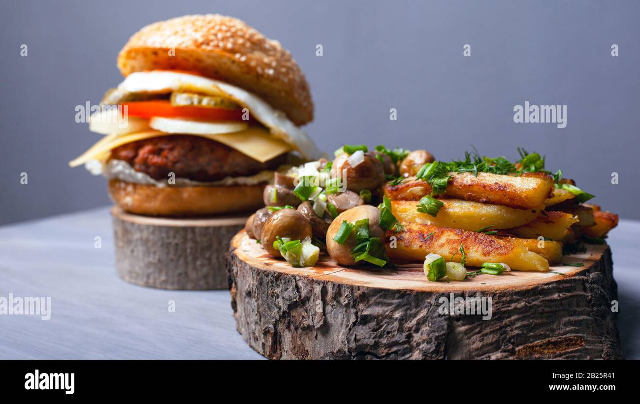 patate fritte con funghi e un hamburger succoso su tavole di legno foresta. home fast food. Foto Stock