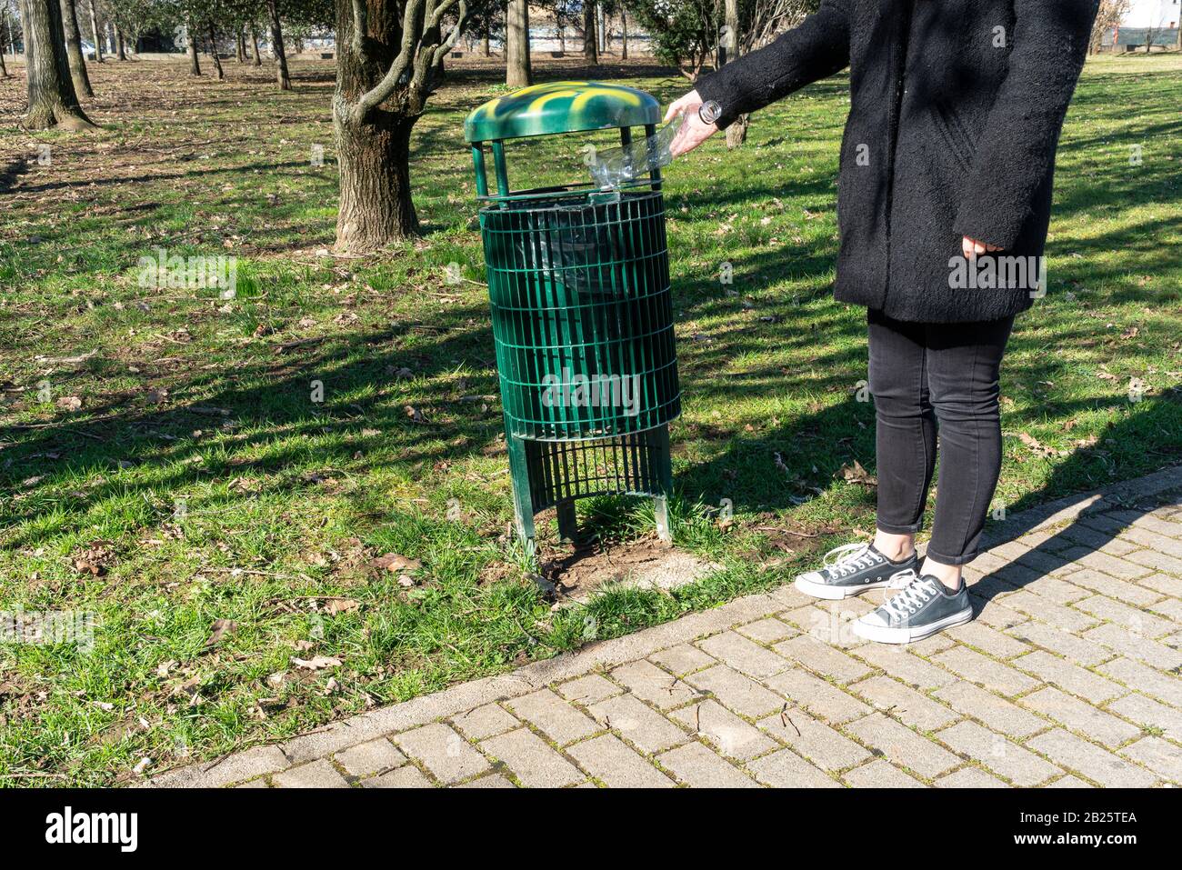 una ragazza raccoglie a terra una bottiglia di plastica e la getta in un cestino di rifiuti Foto Stock