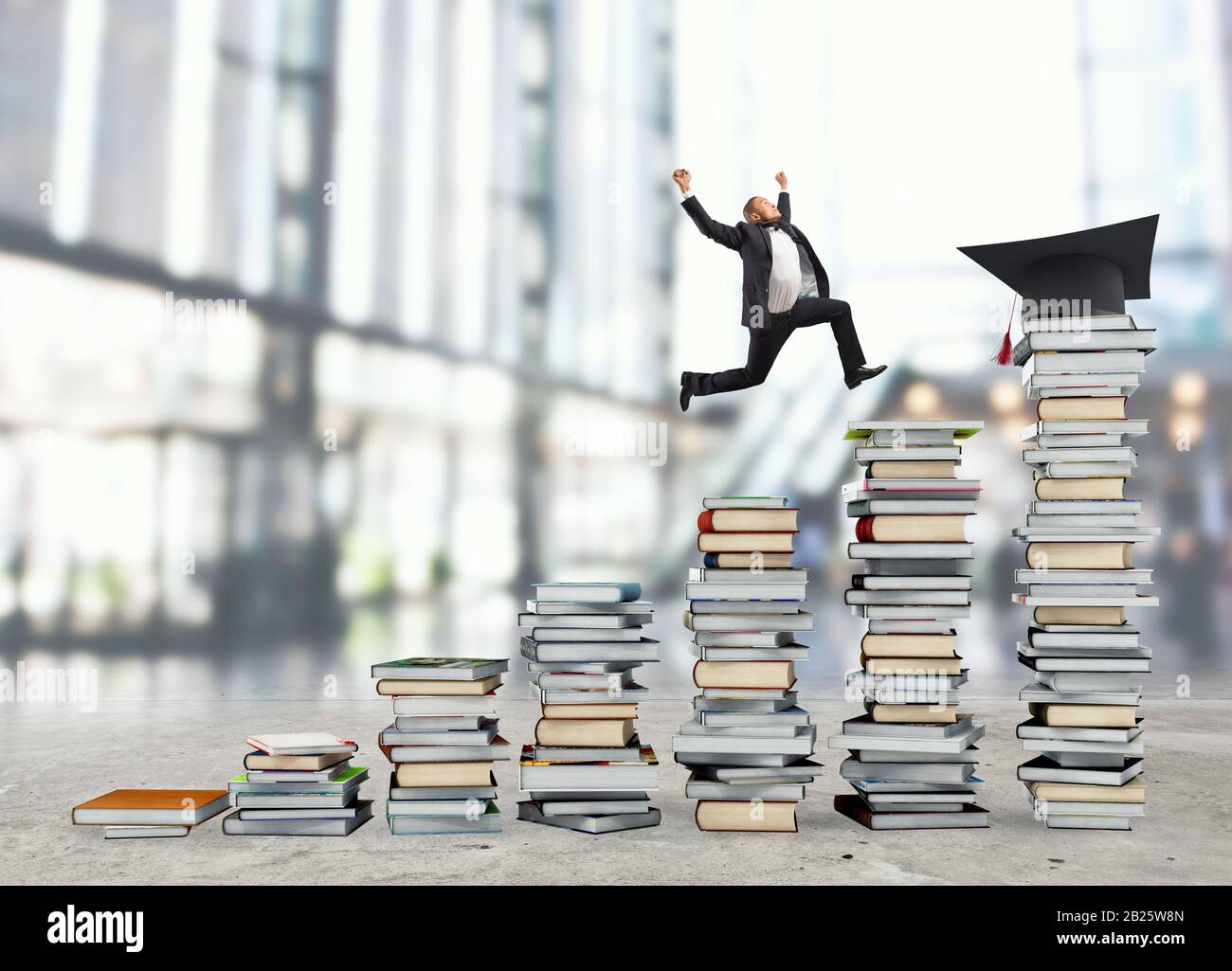 L'uomo d'affari raggiunge il cappello di laurea saltando su mucchi di libri. Concetto di successo e determinazione sullo studio Foto Stock