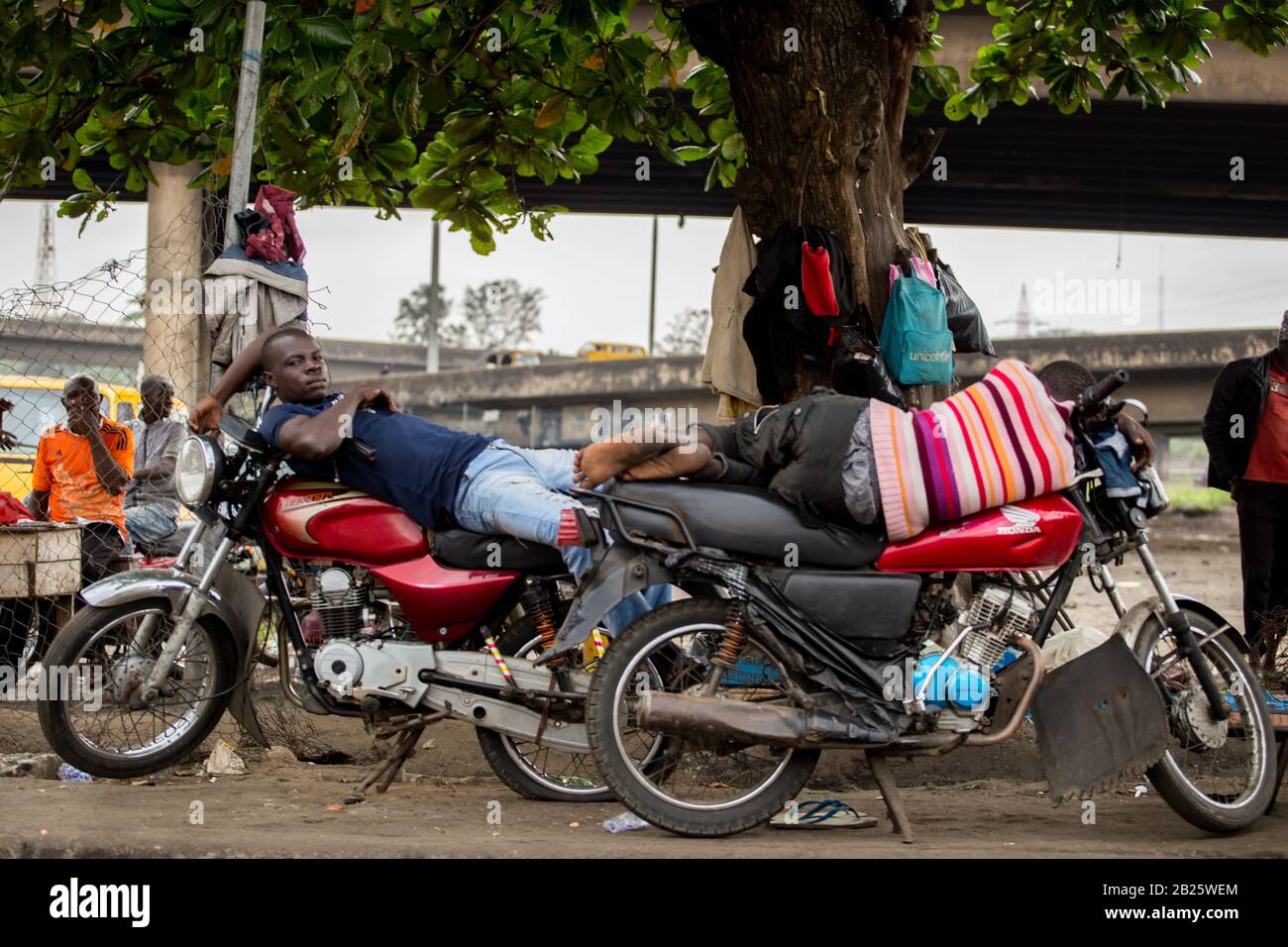 I tassisti del motociclo (okada) prendono un pisolino sulle loro bici in Nigeria. Foto Stock