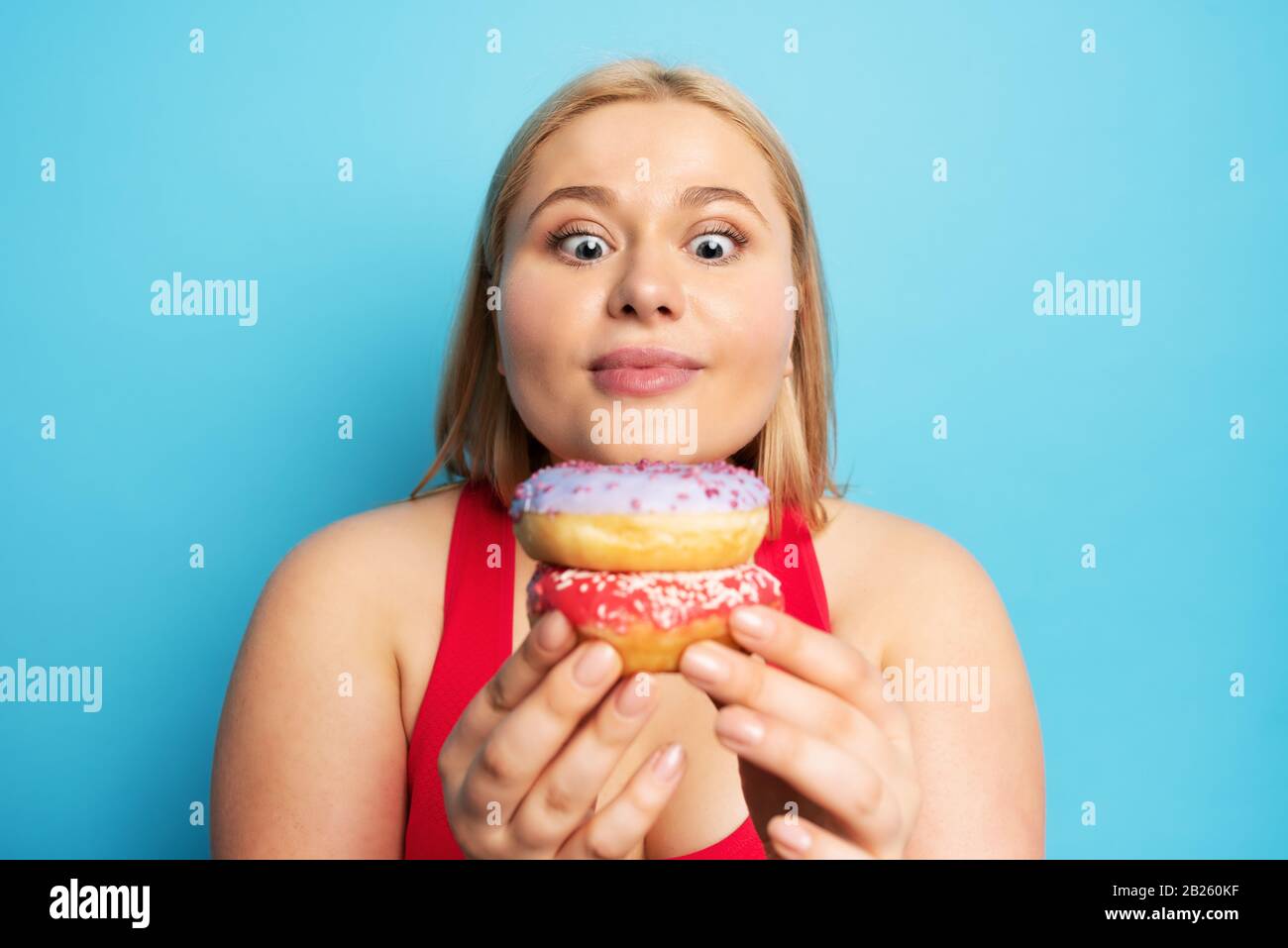 Fat ragazza pensa di mangiare ciambelle invece di fare palestra. Concetto di indecisione e dubbio Foto Stock