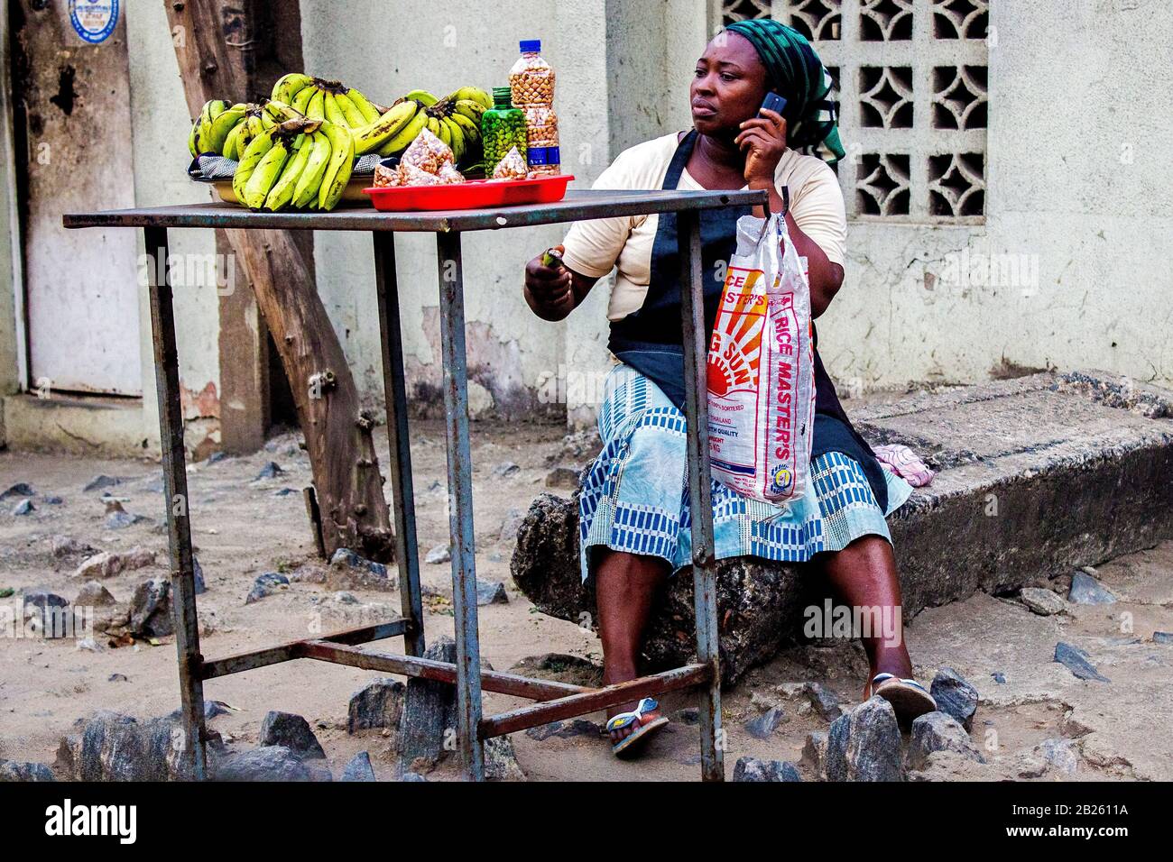 Un fornitore di banane e arachidi fa una chiamata mentre vende su una strada a Lagos, Nigeria. Foto Stock