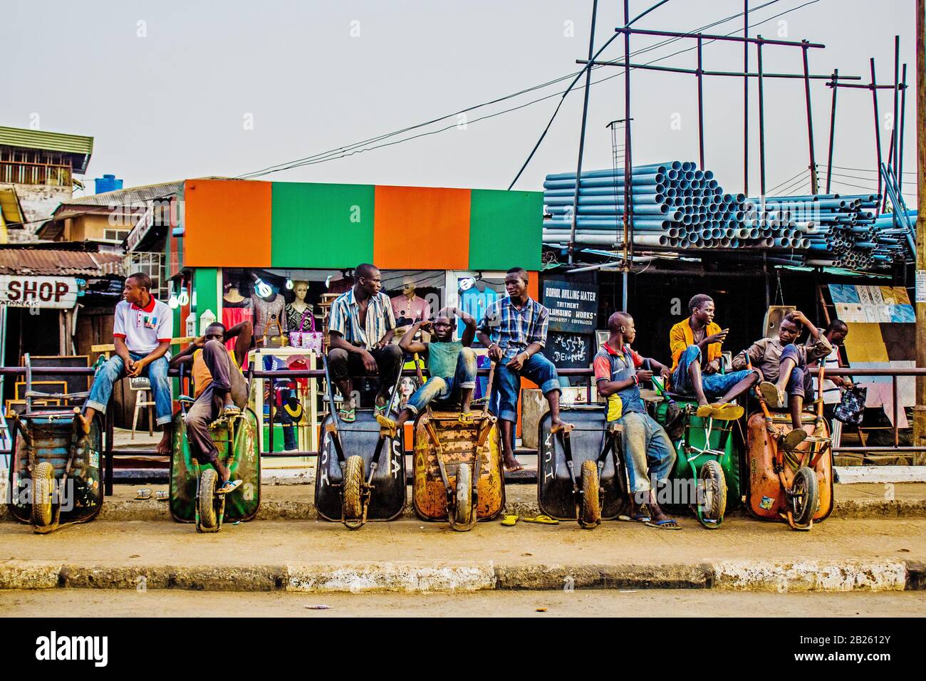 I giovani si siedono sulla carovana che usano per aiutare gli uomini del mercato a trasportare le loro merci mentre aspettano i clienti su una strada a Lagos, Nigeria. Foto Stock