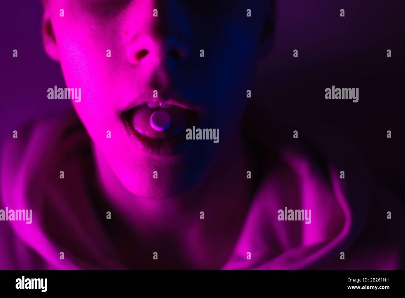 Giovane adolescente in una felpa con cappuccio rosa prende una droga in pillole. Tipo di timone con ruota lsd. Foto Stock