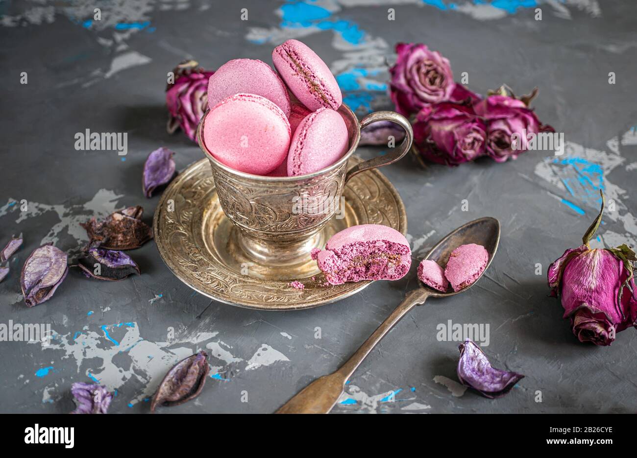 Macaroni di frutta rosa e cioccolato in vaso d'argento su un vecchio tavolo di legno con romantici fiori rosa. Foto Stock