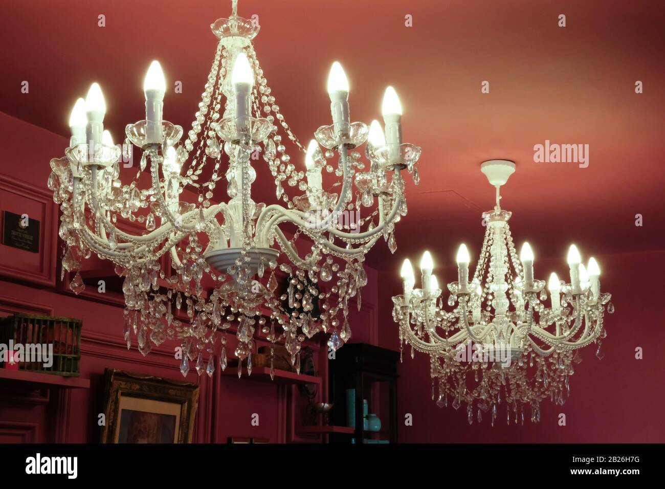 Lampadari bianchi in cristallo finto e candele appesi a un soffitto dipinto di rosso Foto Stock