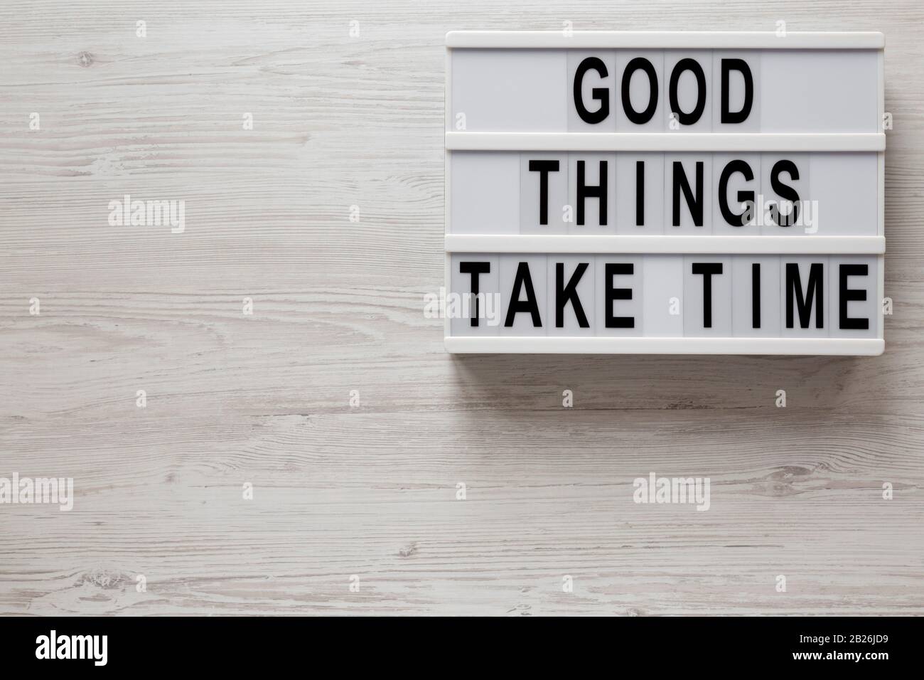 Parole "cose buone prendono tempo" su una scatola moderna su uno sfondo di legno bianco, vista dall'alto. Sopra, dall'alto, disposizione piana. Spazio per il testo. Foto Stock