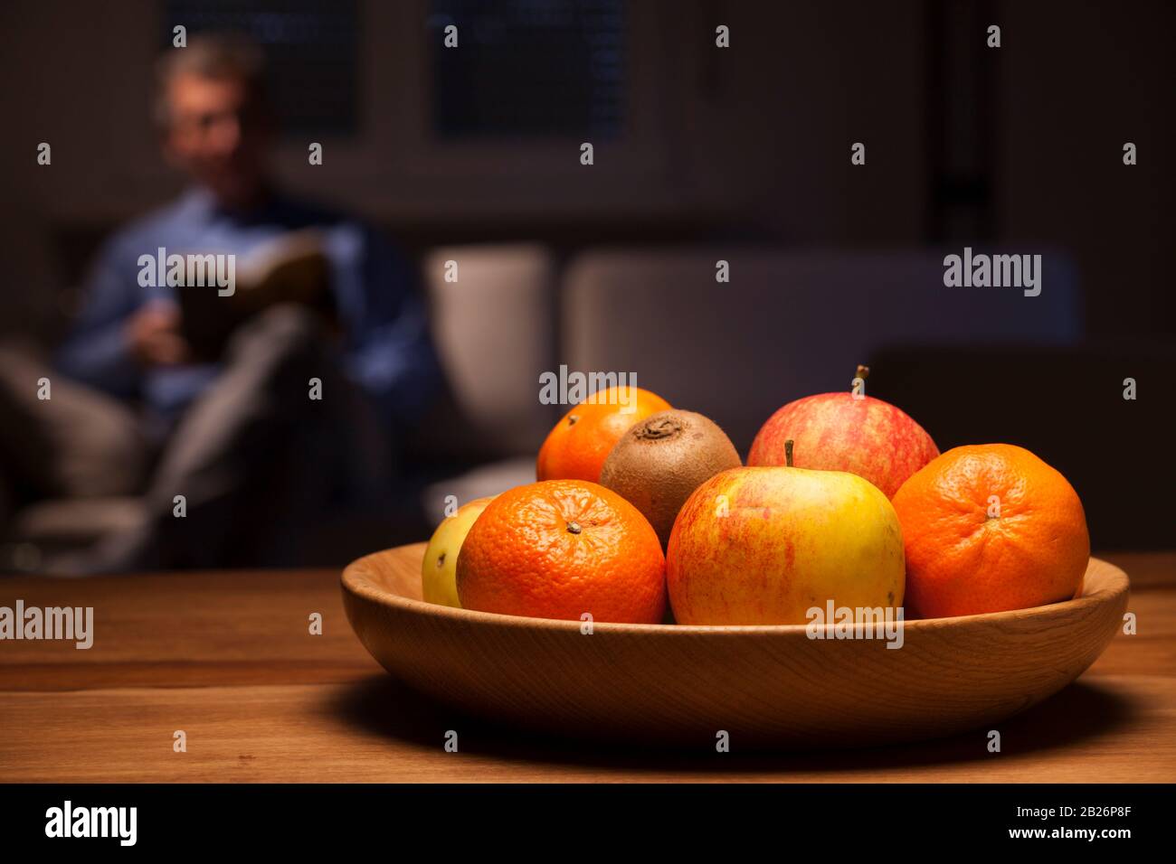 Ciotola di frutta su un tavolo con un uomo che legge su un divano sullo sfondo Foto Stock