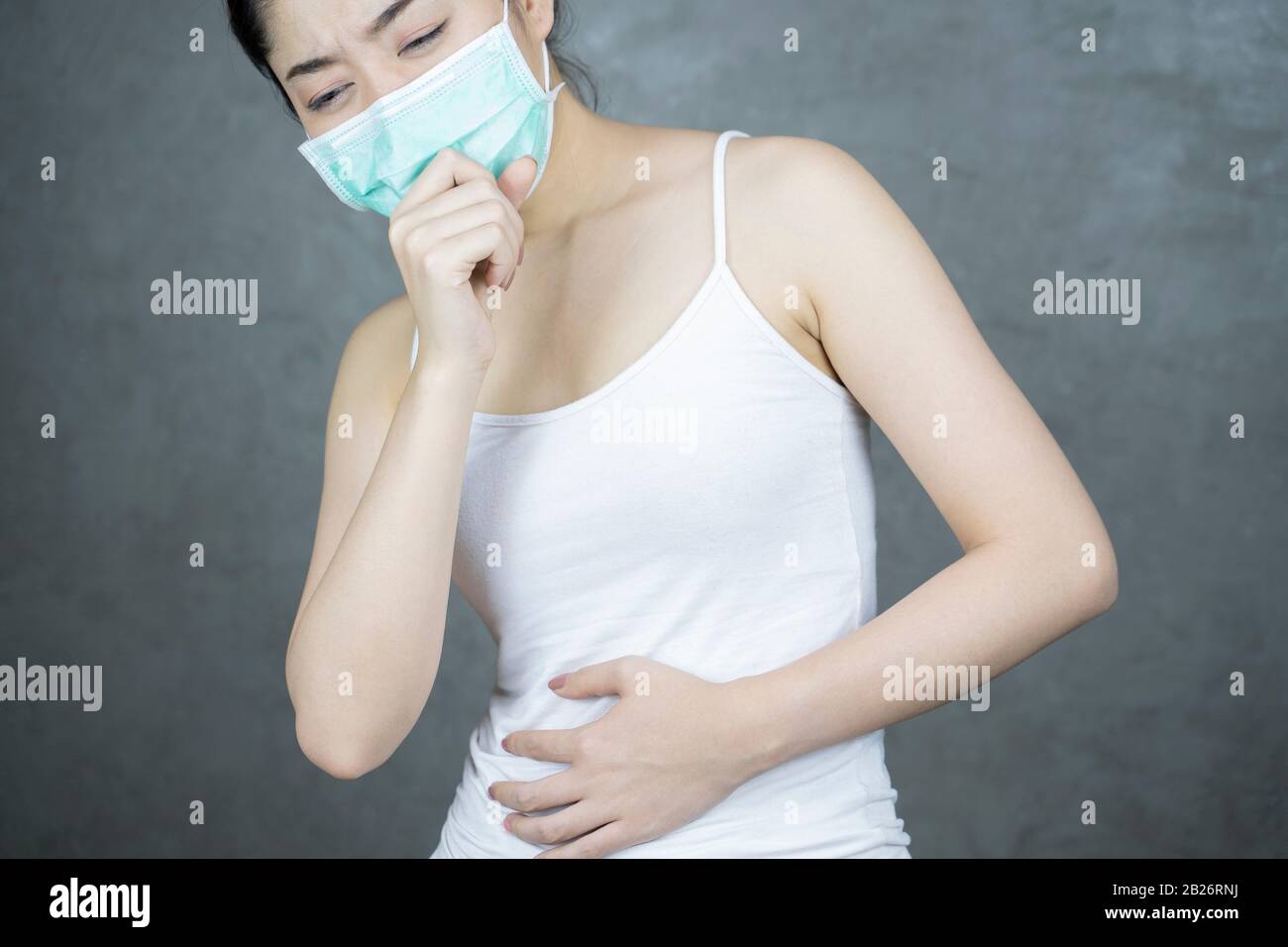 Una donna asiatica che ha un freddo e tosse. Ragazza con maschera protettiva o Igienica in piedi per Virus su sfondo grigio chiaro parete. Spazio di copia. Ilne Foto Stock