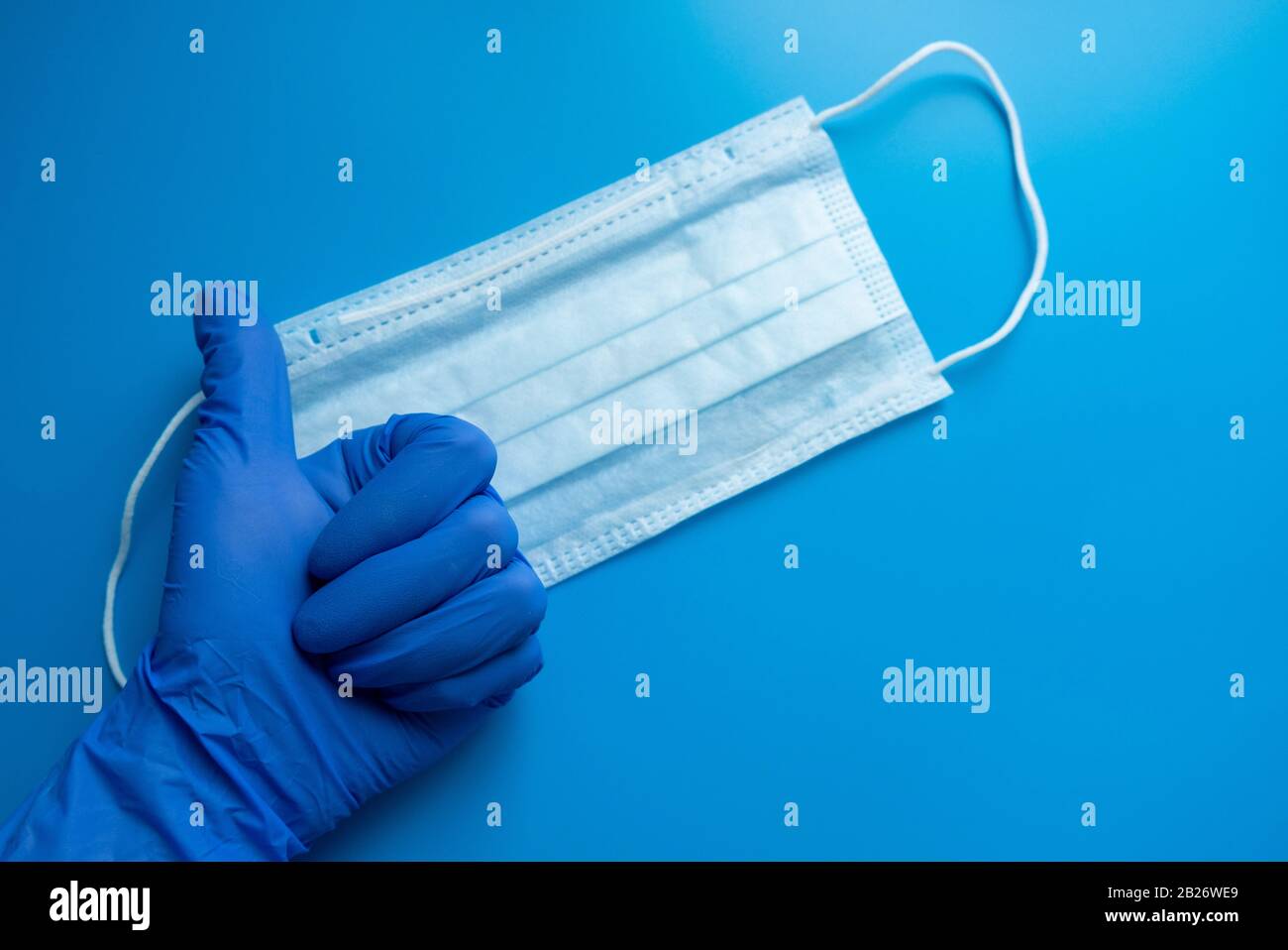 Indossare la maschera protettiva sul fondo blu del guanto per uso medico. Una tipica maschera chirurgica a 3 strati per la copertura della bocca e del naso. Il concetto di pro Foto Stock