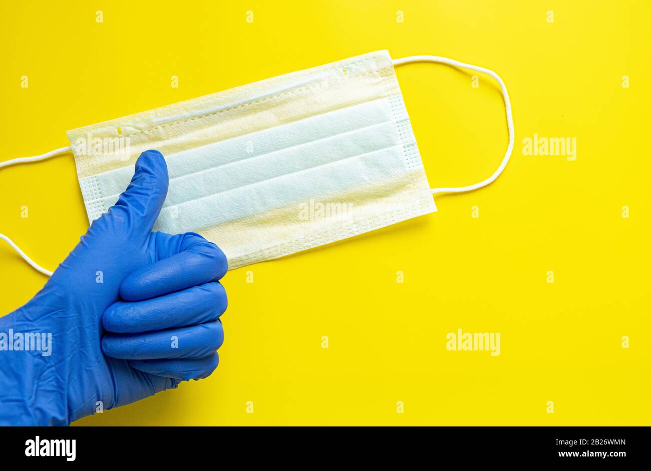 Indossate un guanto per uso medico su uno sfondo giallo con una maschera protettiva per uso medico. Concetto di protezione contro il coronavirus Foto Stock