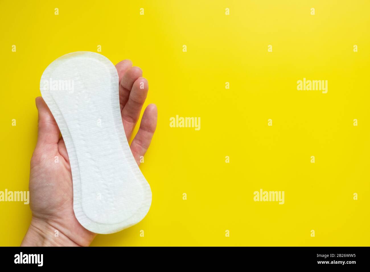 Mano della donna che tiene un assorbente igienico quotidiano su uno sfondo giallo luminoso primo piano dello spazio della copia Foto Stock