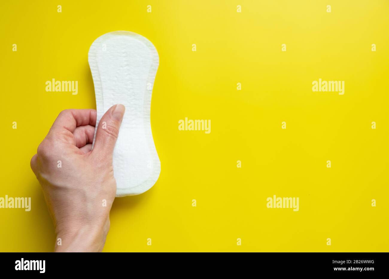 Mano della donna che tiene un assorbente igienico quotidiano su uno sfondo giallo luminoso primo piano dello spazio della copia Foto Stock