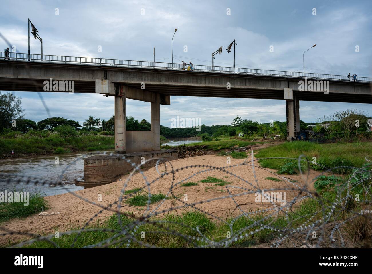 Filo spinato e due persone che camminano attraverso il ponte di amicizia sopra il fiume sul confine Thailandia-Myanmar vicino Mae Sot Foto Stock