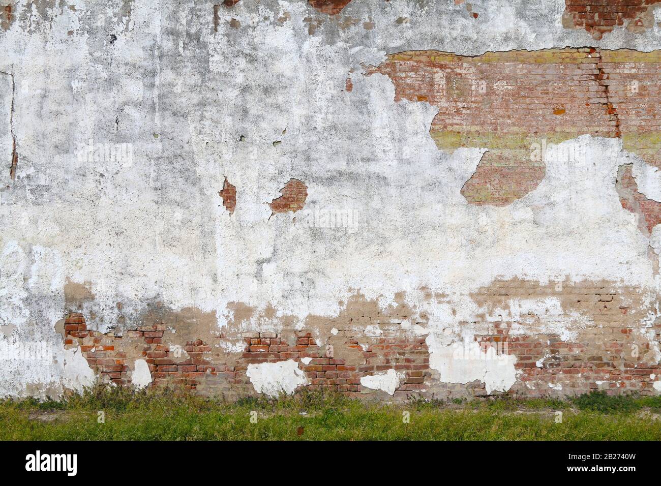 un muro di stucco bianco a vista in cemento e mattoni rossi con erba verge nel pomeriggio Foto Stock