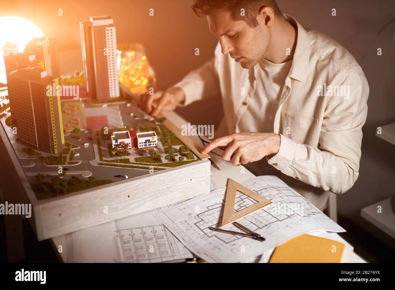 architetto biondo duro lavoro a casa tarda notte, misurando un modello con un righello, seduto al tavolo, primo piano vista laterale foto. Foto Stock
