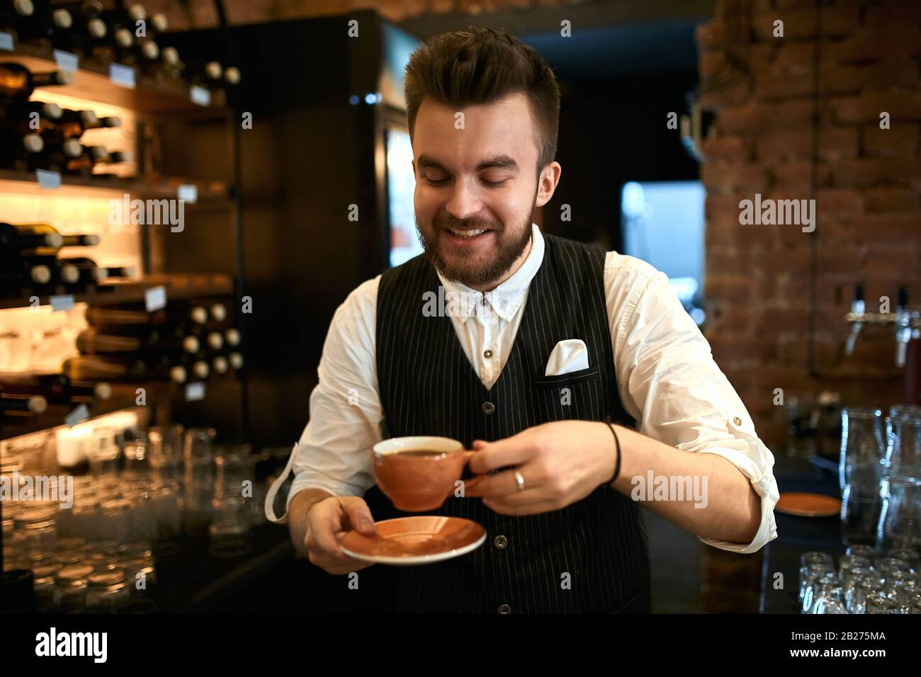 L'uomo allegro è bravo a preparare e servire una varietà di bevande da caffè, foto da vicino. Il preferito job.Barista sorride esprime piacere e presente Foto Stock