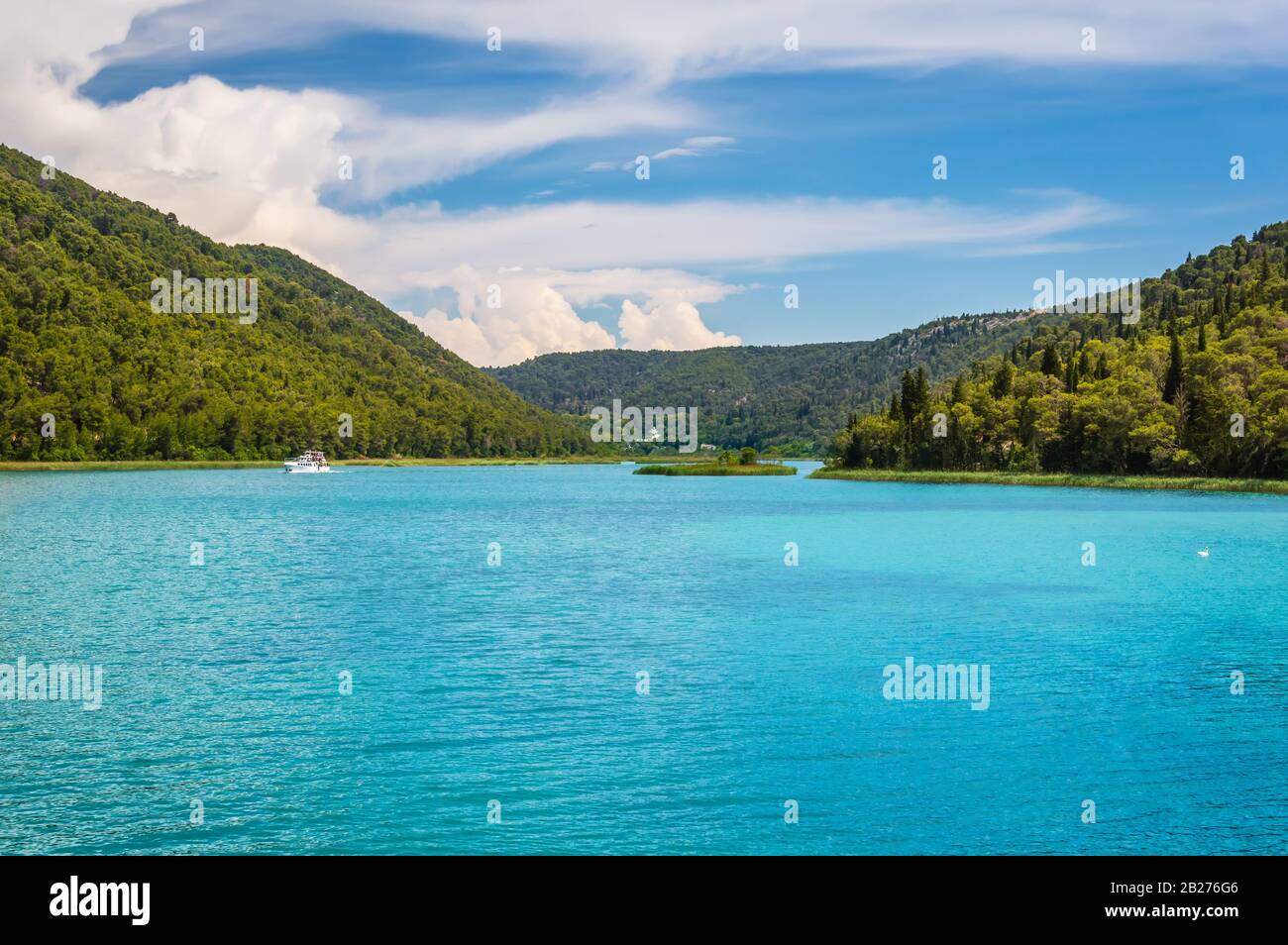 Verdi colline con foresta intorno al fiume Krka nel bellissimo Parco Nazionale di Krka, Croazia. Barche turistiche vela lungo il fiume per arrivare Skradinski buk Waterfal Foto Stock