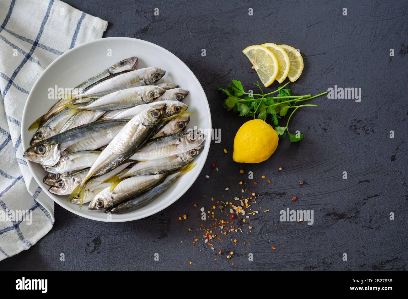 Delizioso pesce fresco, erbe aromatiche, spezie e limone sullo sfondo nero. Cucina mediterranea. Vista dall'alto. Sano e concetto alimentare di dieta. fi grezzo Foto Stock