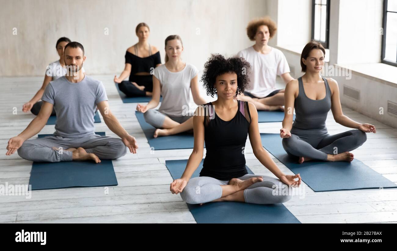 Diversi giovani seduti cross-legged pratica meditazione insieme interni Foto Stock