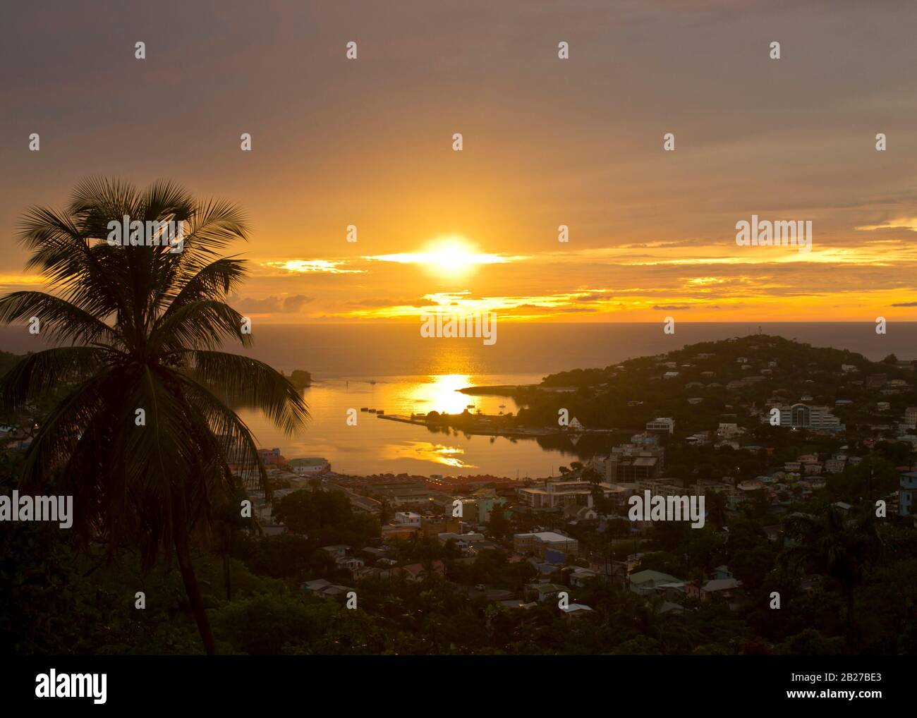 Foto di un luminoso e bellissimo tramonto sulla città con edifici bassi vicino a un porto marittimo vuoto con riflessi del sole sull'acqua e palme isolate a sinistra Foto Stock