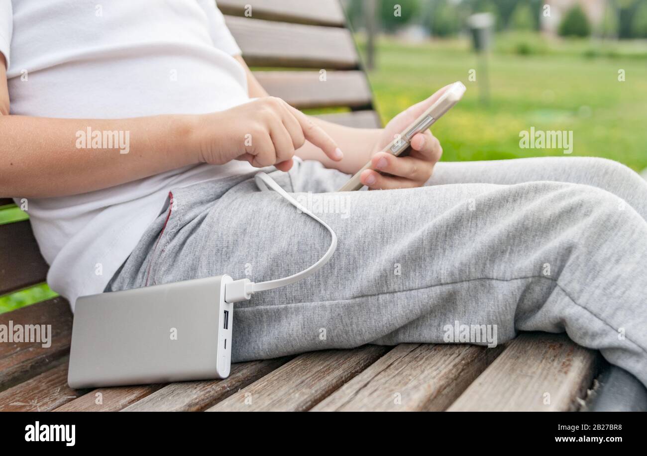 Ragazzo che utilizza il telefono sul banco durante la ricarica dal power bank. Foto Stock