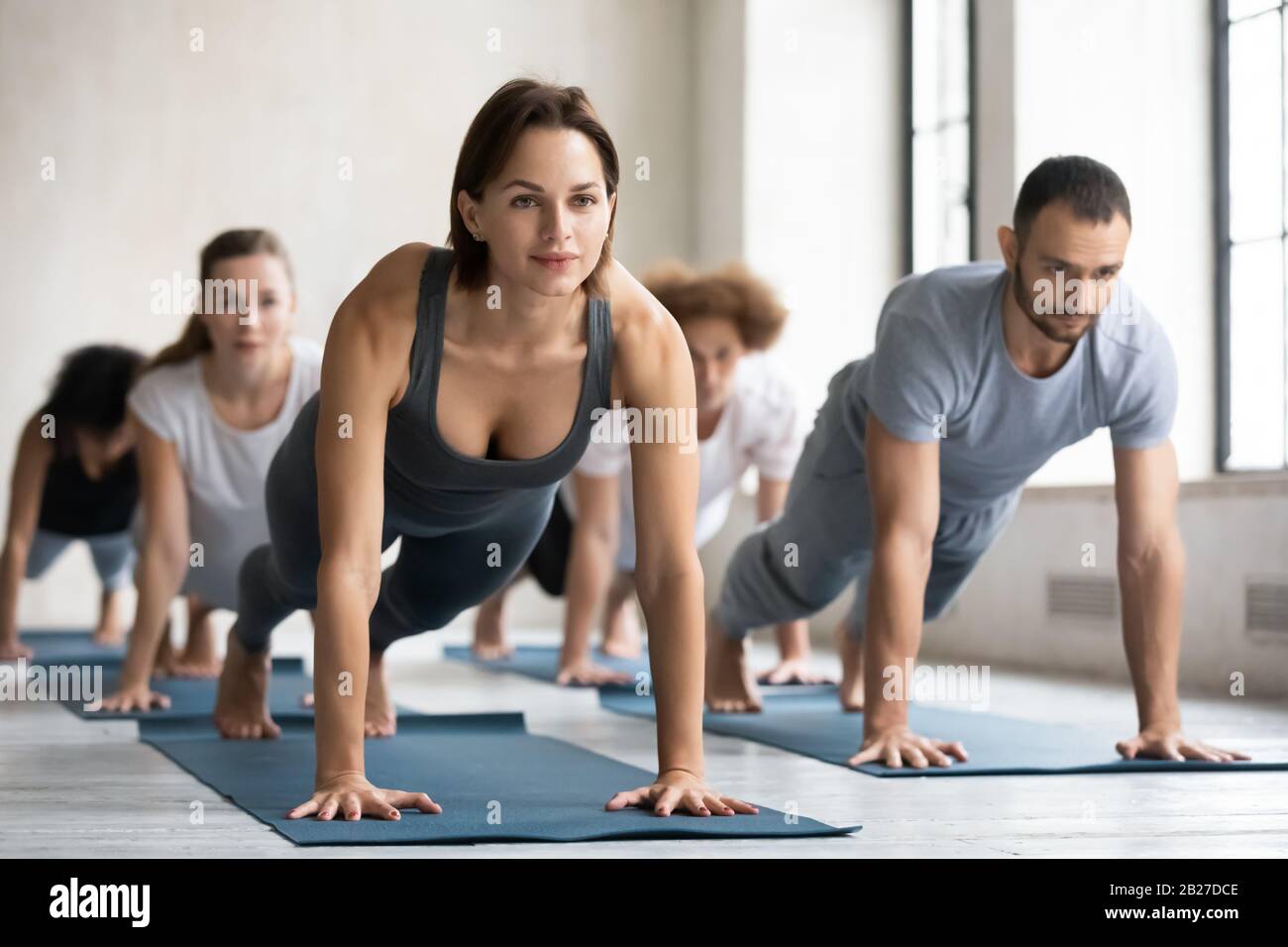 Donna allenatore e gruppo di persone che si esibiscono insieme plank posa Foto Stock