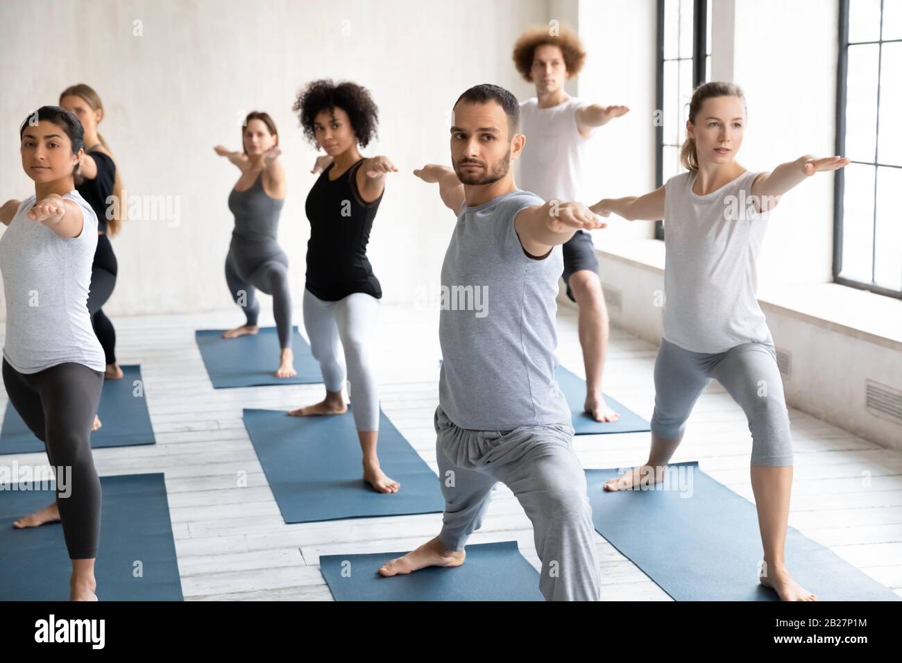 Sette persone multietniche principianti praticando yoga eseguendo Warrior II posa Foto Stock