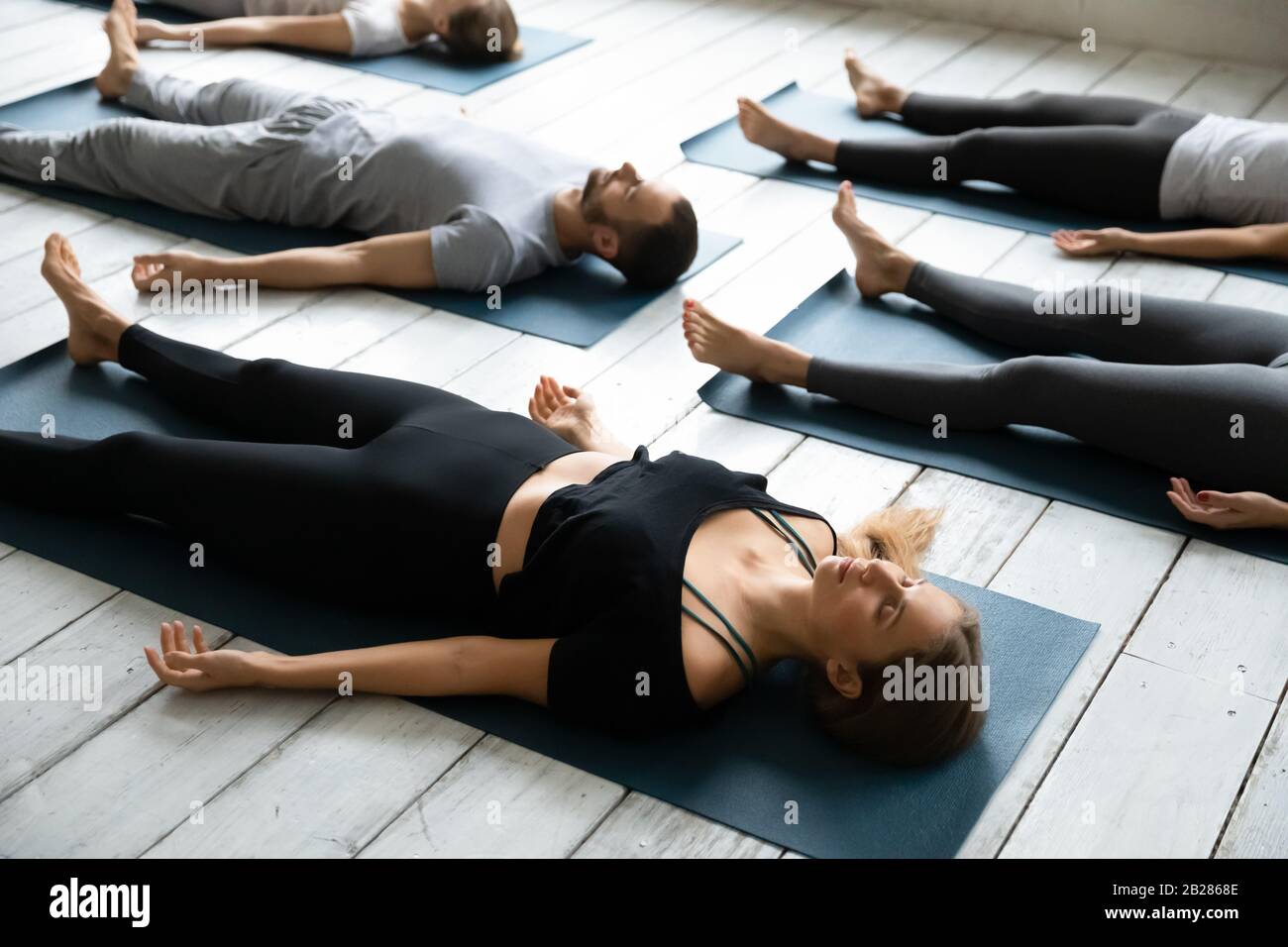 La gente riposa dopo l'allenamento di yoga che giace nella Posa di Shasvasana Foto Stock