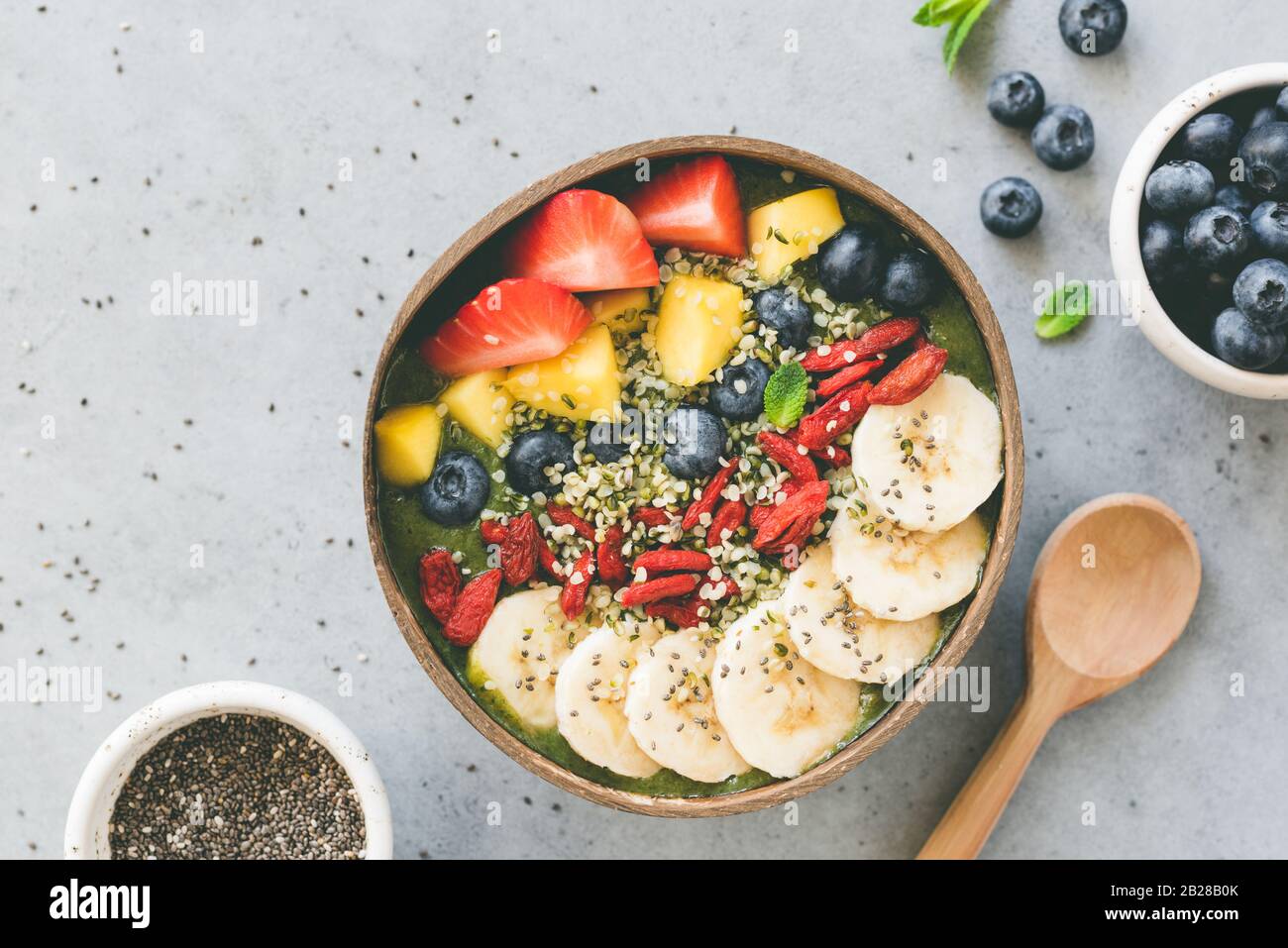 Frullato superfood crudo in ciotola di cocco con superfood condimenti semi di canapa, semi di chia, frutti di bosco di goji banana di mango mirtillo e fragola Foto Stock