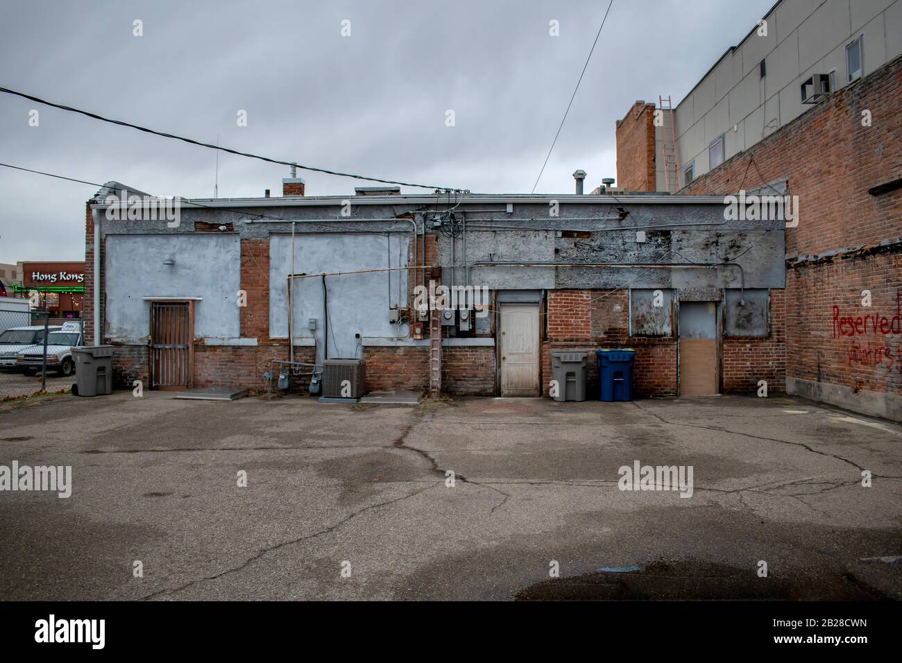Parte posteriore di un vecchio edificio del centro cittadino con tre porte agli stabilimenti interni con lattine di calcestruzzo fessurato e sporco deteriorarsi mattoni rossi exte Foto Stock