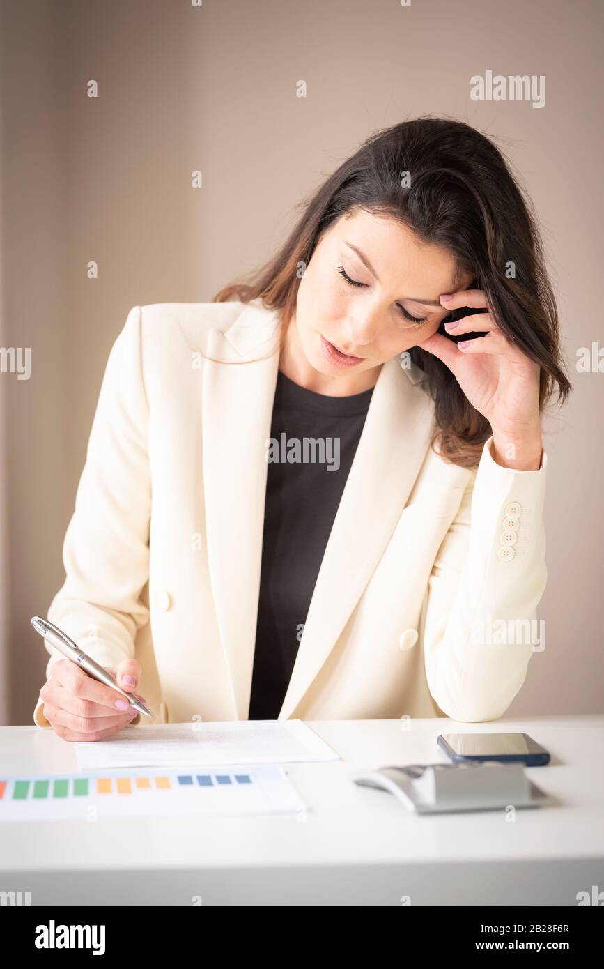Colpo di donna d'affari careusura seduta alla scrivania e guardando thougtfully mentre fa un certo lavoro di ufficio. Foto Stock