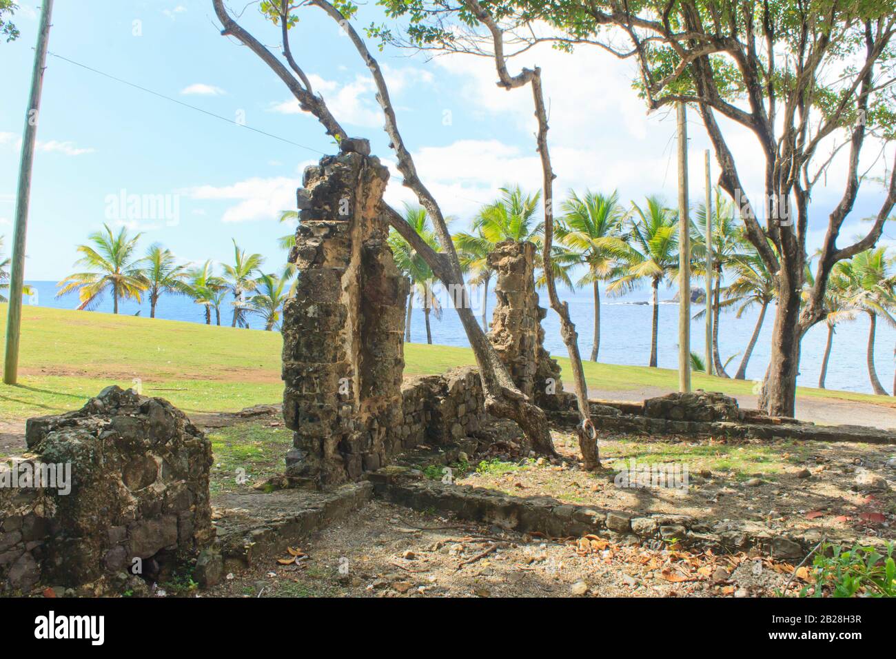 Vecchia struttura coloniale in mattoni sui terreni erbosi dell'isola di Pigeon dove gli alberi ora crescono e le palme da cocco, il cielo blu luminoso con le nuvole bianche Foto Stock