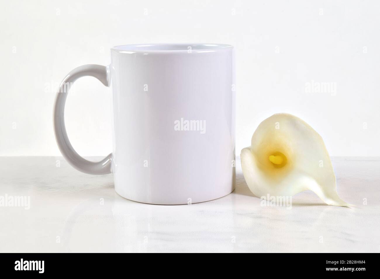 Tazza bianca bianca vuota con una tazza da 11 once accanto a un bellissimo ciglio bianco di Pasqua Calla. Foto Stock