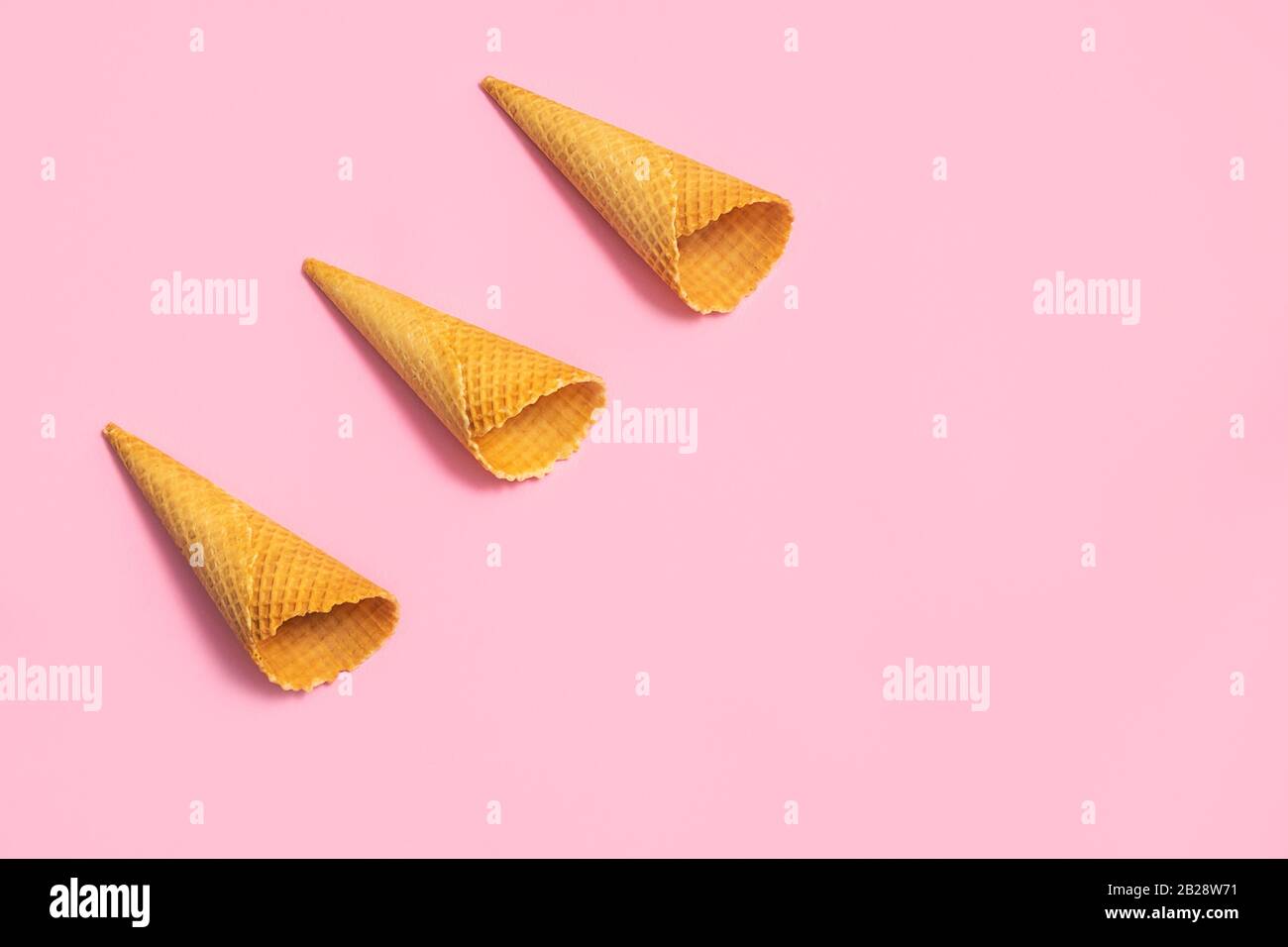 Coni gelato vuoti su morbido fondo rosa. Disposizione piatta con spazio di copia, motivo Foto Stock