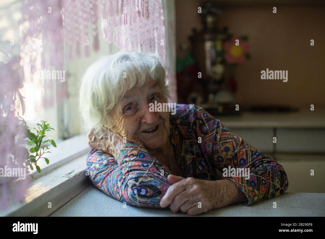 Ritratto di una vecchia donna seduta a un tavolo in casa. Foto Stock