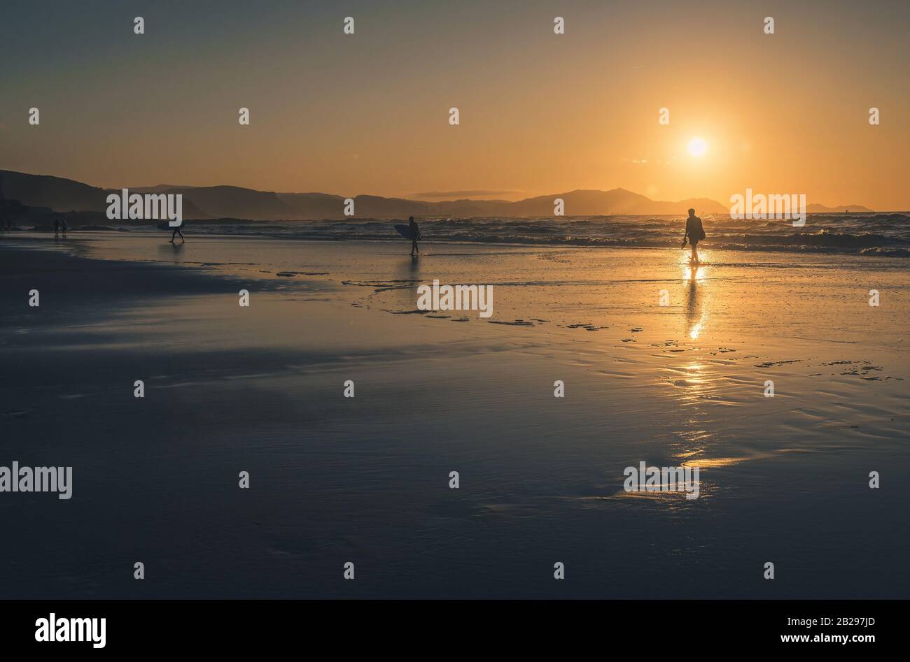 Silhouette di surfista persone che portano la loro tavola da surf sulla spiaggia al tramonto sulla riva del mare vicino a Bilbao in Spagna. Filtro vintage Foto Stock