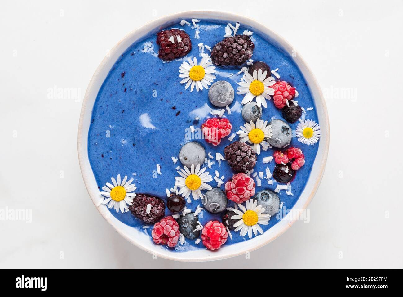 ciotola smoothie blu spirulina con frutti di bosco freschi e congelati, fiori di cocco e camomilla. salutare dessert per la colazione. vista dall'alto Foto Stock