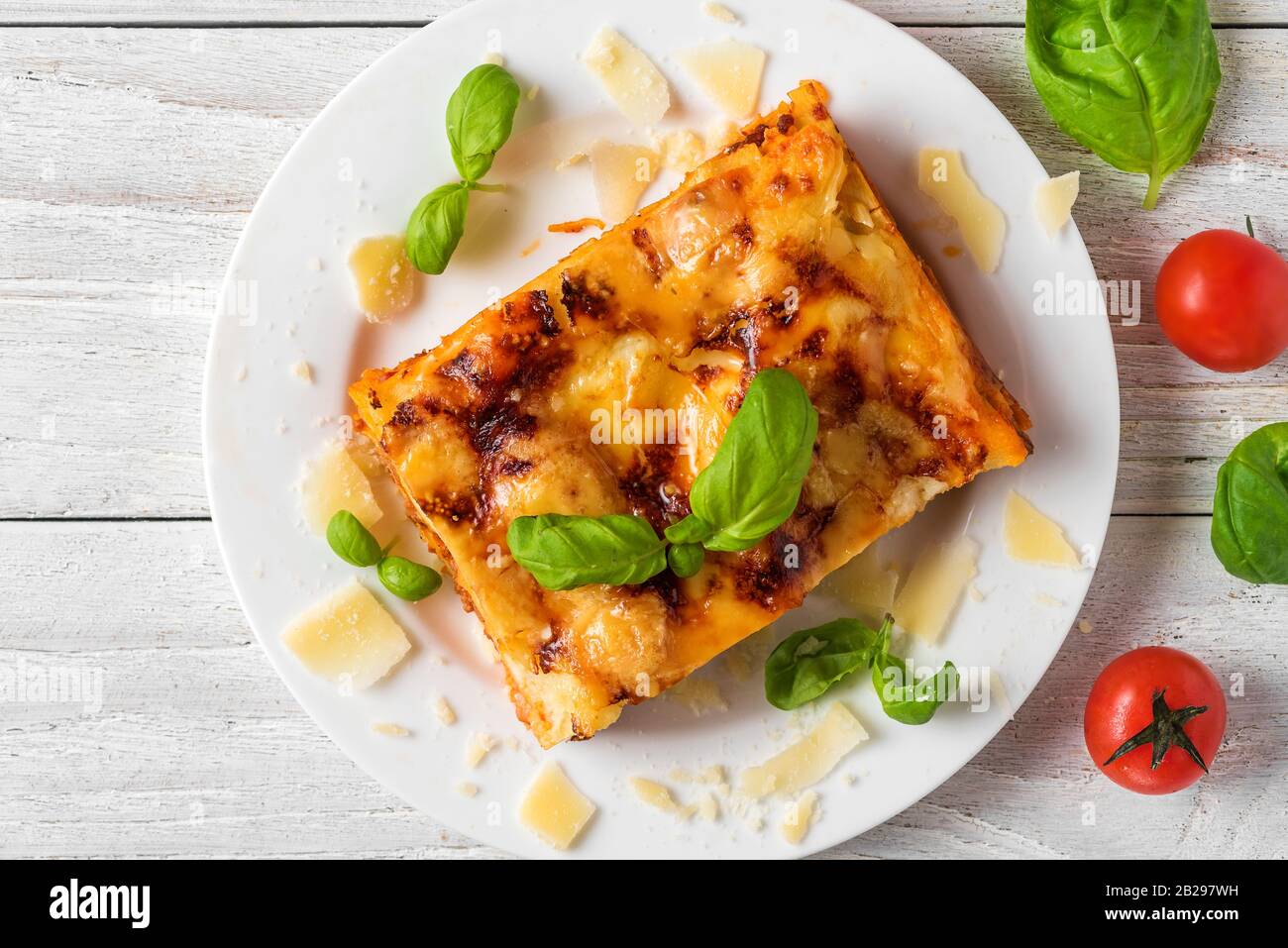 Lasagne di carne con basilico fresco e parmigiano in un piatto su un tavolo di legno bianco. Vista dall'alto. Cibo italiano. Foto Stock