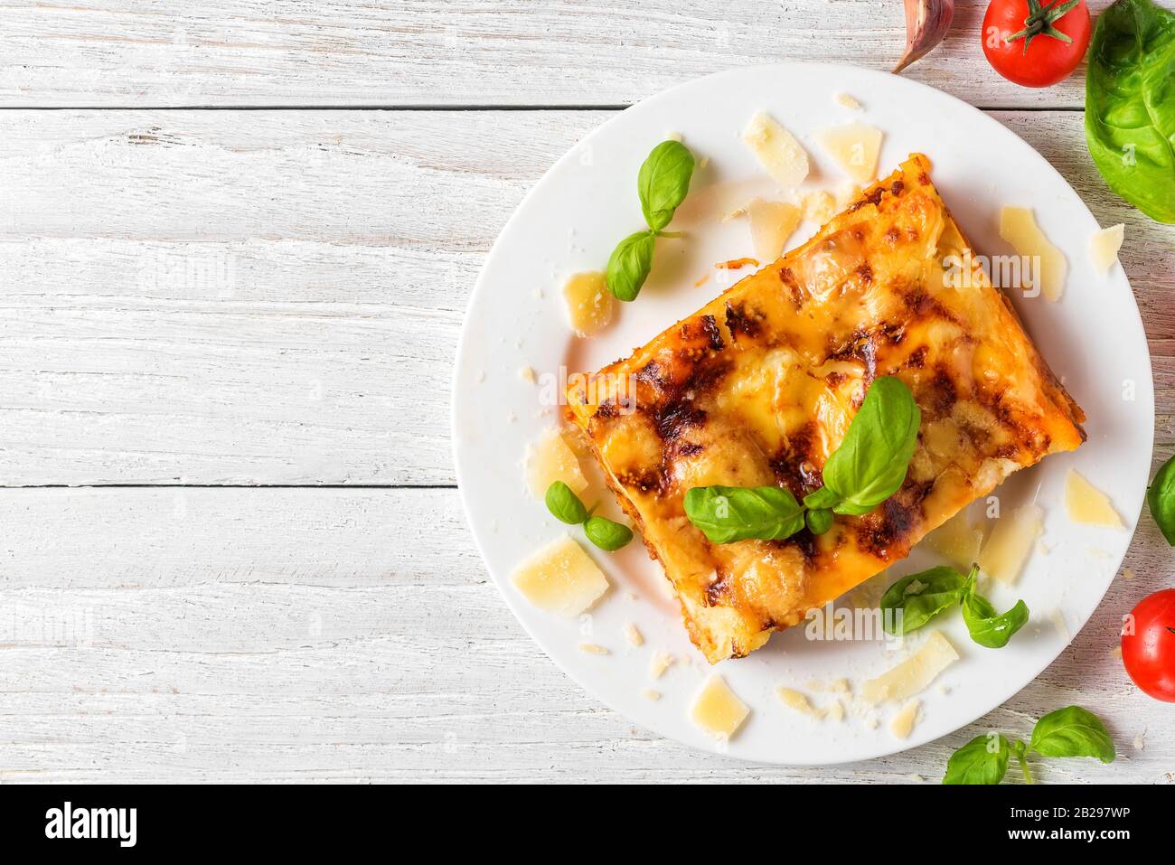 Lasagne di carne fatte in casa con basilico fresco e parmigiano in un piatto su un tavolo di legno bianco. Vista dall'alto. Cibo italiano. Foto Stock