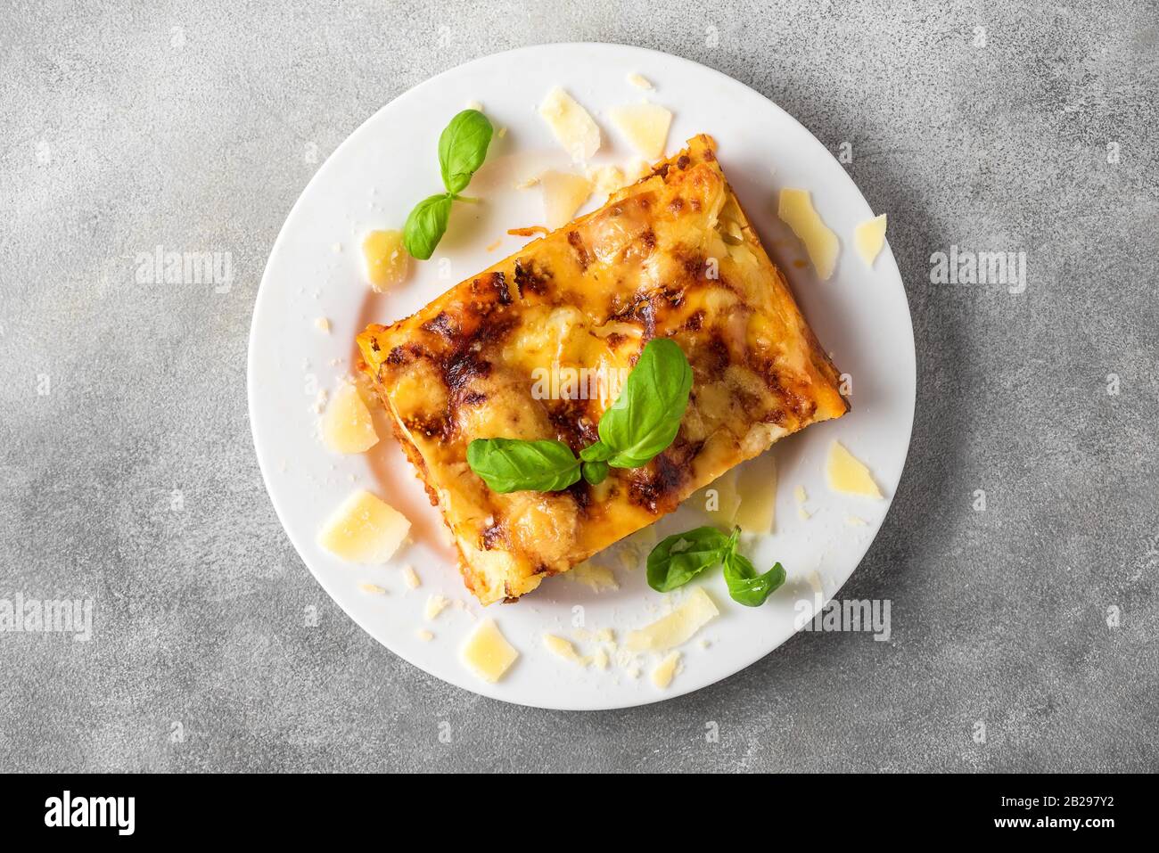 Lasagne di carne fatte in casa con basilico fresco e parmigiano in un piatto su fondo grigio in cemento. Vista dall'alto. Cibo italiano. Foto Stock