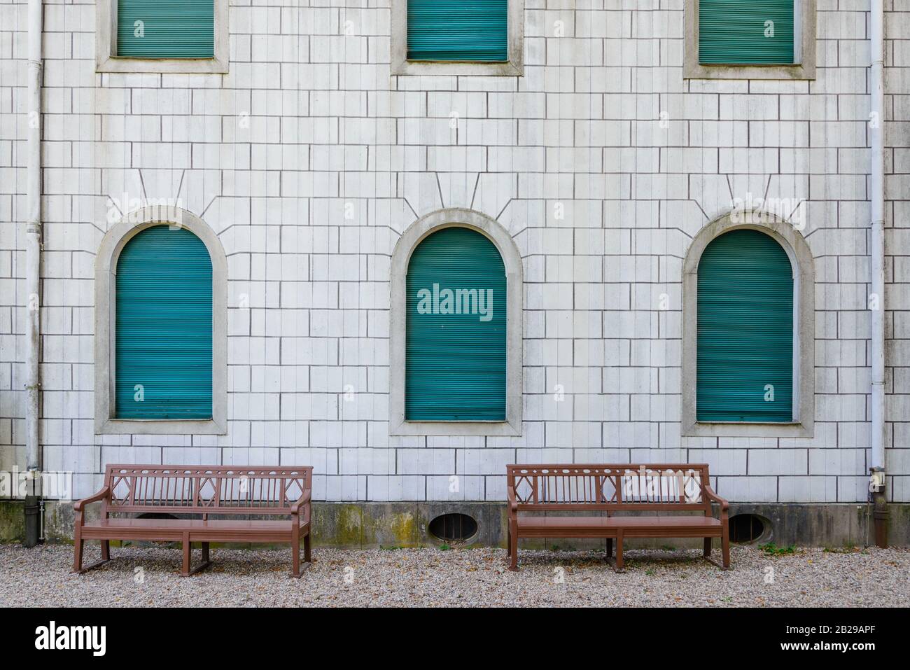 Facciata esterna con pareti in pietra bianca, finestre verdi ad arco e panca in legno. Foto Stock