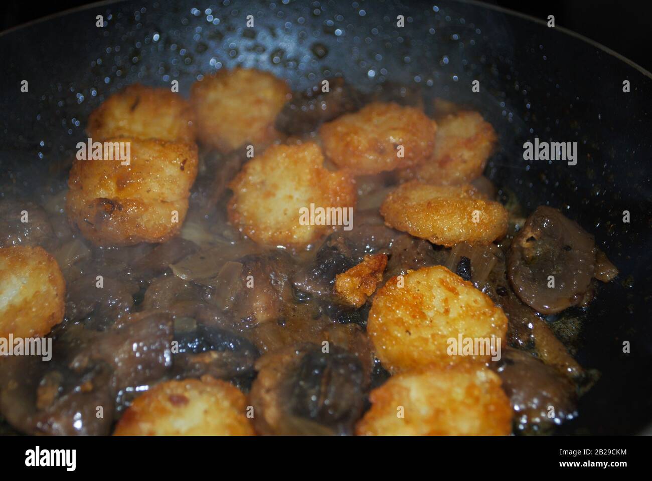 cottura dei funghi cipolle e crocchette di patate in una padella con olio condimento e vapore Foto Stock