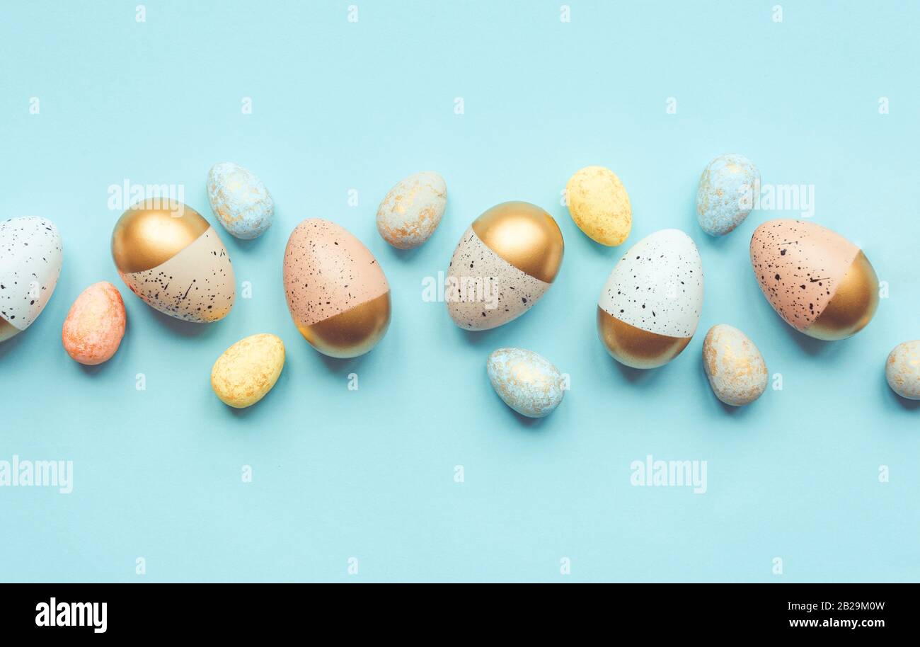Vista dall'alto delle uova di Pasqua colorate con vernice dorata e colori diversi. Sfondo blu. Spazio di copia. Foto Stock