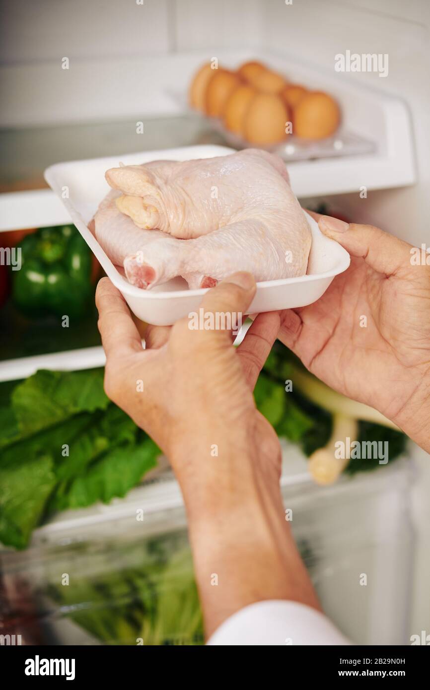 Mani di persona che prende freddo tights di pollo fuori dal frigorifero quando cucinano la cena a casa Foto Stock