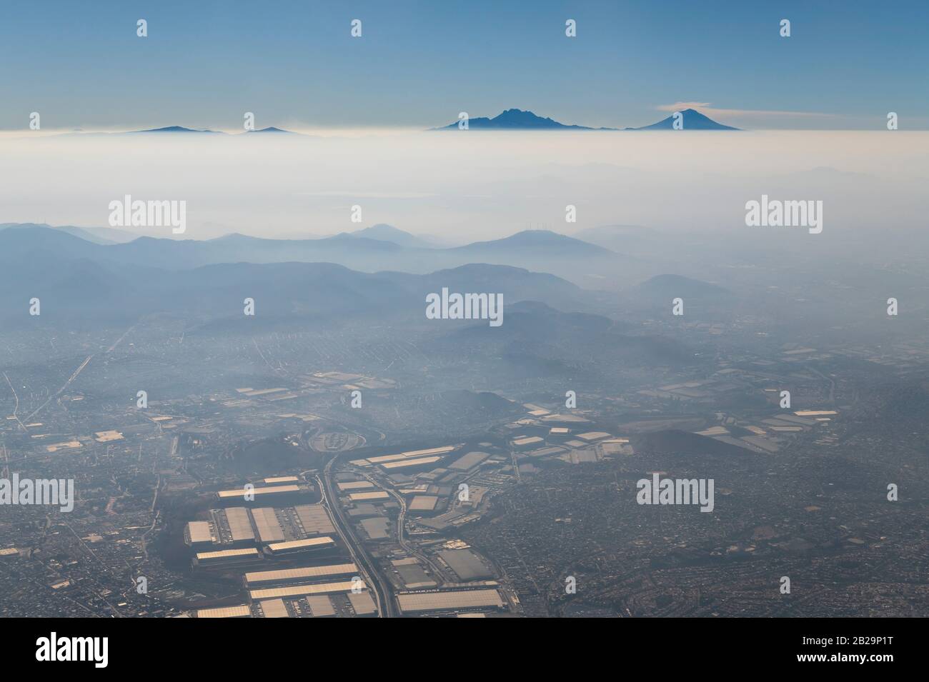 Veduta aerea di Città del Messico nello smog e nebbia con il Popocatepetl attivo e dormiente Iztaccihuatl vulcano all'orizzonte, Messico. Foto Stock