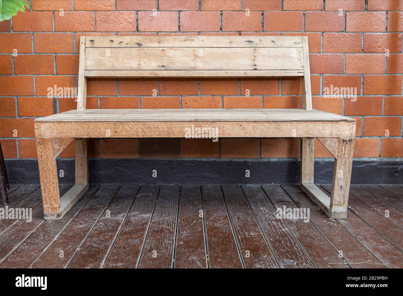 Panca di legno su pavimento di legno con sfondo di piastrelle rosse sulla terrazza. Foto Stock